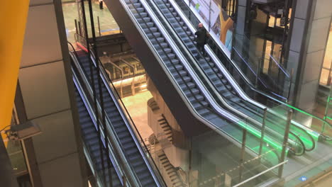 A-man-riding-an-escalator-in-a-modern-hall,-another-descending-with-an-elevator,-modern-construction-and-architectural-design,-metal-and-concrete-architecture