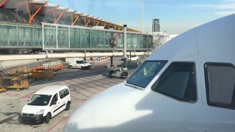 Nose-of-modern-airliner,-a-passenger-boarding-bridge-in-background,-people-boarding-an-airplane,-service-vehicles-on-tarmac,-transportation-and-travel-concept,-Madrid-Barajas-Airport