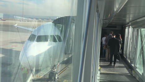 Panning-shot-from-passenger-boarding-bridge-with-airliners-on-tarmac,-people,-unrecognizable,-waiting-to-board-the-plane,-travel,-business-and-transportation-concept,-Madrid-Barajas-Airport-in-Spain