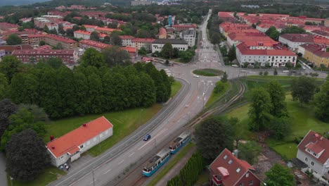 Aerial-view-of-the-roundabout-at-Munkebackstorget-in-east-Gothenburg-in-Sweden-with-a-blue-tram-driving-in-towards-the-stop-with-lots-of-apartement-buildings-around-it-and-some-greenery