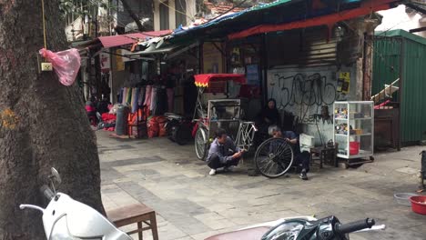 Hombres-Trabajando-Y-Arreglando-Ruedas-De-Carro-En-La-Acera-En-Hanoi,-Vietnam