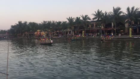 Überfülltes-Boot,-Das-Entlang-Des-Flusses-In-Der-Nähe-Einer-überfüllten-Vietnamesischen-Stadt-Schwimmt