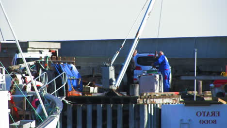 Hombres-Trabajando-En-Un-Muelle-En-Un-Puerto-Deportivo-Operando-Un-Polipasto-Utilizado-Para-Cargar-Equipos-Y-Suministros-En-Barcos-Cercanos.