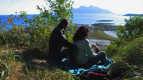 A-couple-sits-on-a-hilltop-overlooking-the-sea-below-as-leaves-blow-in-a-gentle-breeze