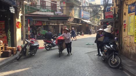Woman-walking-bike-and-food-down-alley-in-Hanoi,-vietnam