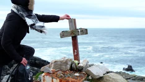 Female-placing-stone-on-Malin-head-wooden-cross-shrine,-Northern-Ireland-coastal-tourist-interesting-public-attraction