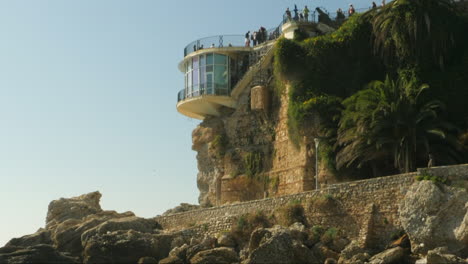 Blonde-walks-down-sand-beach,-tourist-stand-on-Balcon-de-Europa,-Nerja