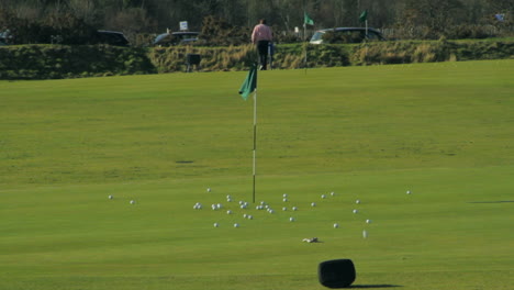 Balls-rolling-towards-hole-under-pole-with-green-flag-on-golf-course-of-St-Andrews