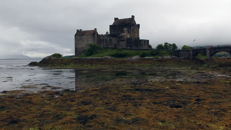 Eilean-Donan-Castle-Drohnenaufnahme-Bei-Sonnenuntergang-An-Einem-Bewölkten,-Launischen-Tag