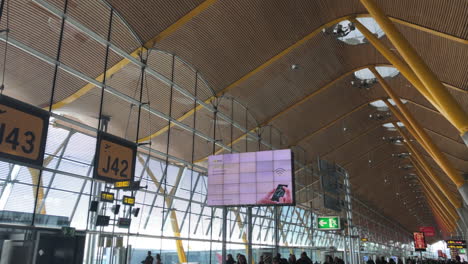 Slow-motion-shot-of-the-interior-of-a-terminal-in-Madrid-airport-with-signs,-billboards-and-gate-numbers