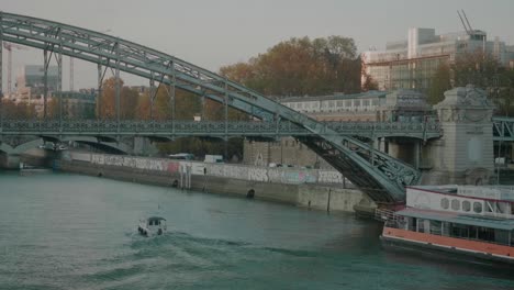 Pequeño-Barco-Pasando-Por-Debajo-Del-Puente-Sobre-El-Río-Sena-Con-Tráfico-Pasando-Al-Lado,-París,-Francia
