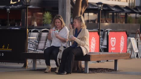 Two-girls-chatting-on-chair-along-boardwalk-in-Newcastle-along-harbour