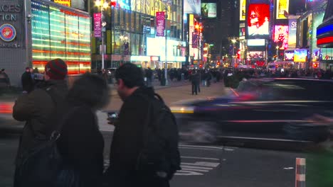 Die-Leute-Bleiben-Stehen,-Um-Sich-Fotografieren-Zu-Lassen-Und-Machen-Selfies-Mit-Den-Berühmten-Lichtern-Und-Werbetafeln-Des-Times-Square-Im-Hintergrund,-Während-Im-Hintergrund-Der-Verkehr-Vorbeirauscht