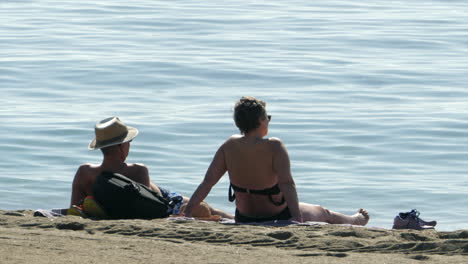 Pareja-Tumbada-En-La-Playa-Bajo-El-Sol,-Fondo-Del-Mar