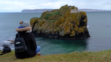 Person,-Die-Auf-Der-Küstenklippe-Irlands-Sitzt-Und-Die-Felsige-Küstenformation-Der-Ozeaninsel-Beobachtet