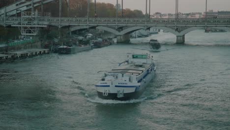 Cargo-Boat-Travelling-Along-River-Seine-In-Paris-With-Bridge-In-The-Background