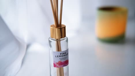 Diffuser-bottle-with-sticks-in-a-pure-white-environment-with-a-green-candle-in-the-background