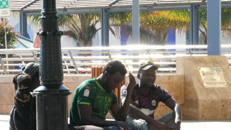 Three-Black-Males-Talking-Sitting-on-the-Sidewalk-on-a-Sunny-Day-SLOMO