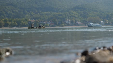 Two-men-rowing-in-a-traditional-wood-canoe-on-the-Danube-near-Zebegeny,-Hungary