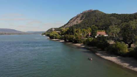 Luftaufnahme-Von-Zwei-Männern,-Die-Flussaufwärts-Auf-Der-Donau-Bei-Visegrad-Kanu-Fahren,-Mit-Der-Burg-Auf-Dem-Hügel-Im-Hintergrund