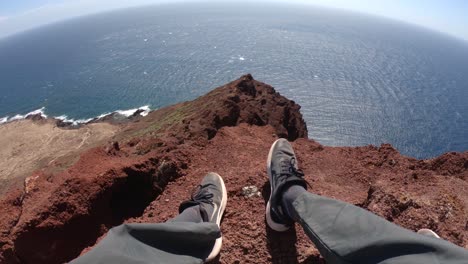 Piernas-De-Excursionista-Sentado-En-El-Borde-De-La-Montaña-Roja-Con-Vistas-Al-Tranquilo-Mar-Azul-En-Tenerife,-España