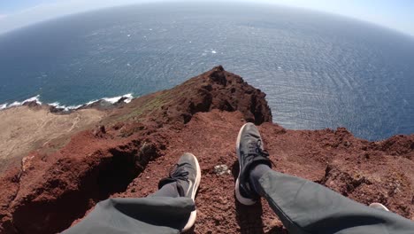 Beine-Eines-Wanderers,-Der-Am-Rande-Der-Montaña-Roja-Mit-Blick-Auf-Das-Ruhige-Blaue-Meer-Auf-Teneriffa,-Spanien,-Sitzt