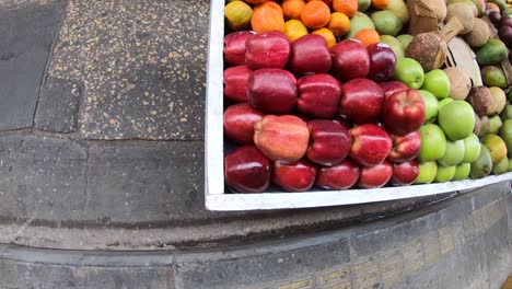 A-cart-wheel-filled-with-apples,-pears,-oranges,-avocado,-oranges-and-other-fruits-is-passing-by-a-street-in-the-old-town-of-Cartagena-de-Indias