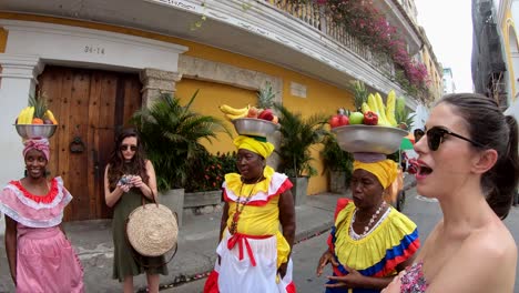 Tourists-are-standing-and-talking-with-palenqueras-with-colorful-dresses-who-are-balancing-bowls-of-fruit-in-their-heads-in-the-old-town-of-Cartagena-de-Indias,-Colombia