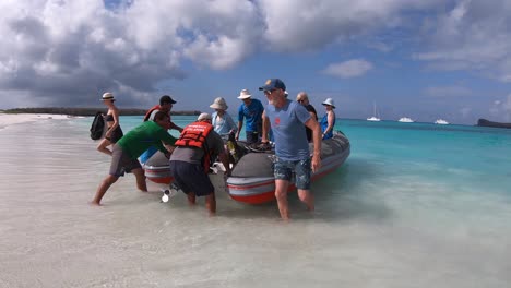 Bootsführer-Halten-Ein-Boot,-Weiße-Touristen-Gehen-An-Einem-Weißen-Sandstrand-Der-Galapagos-Inseln-Von-Bord