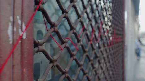 Follow-Shot-Along-Metal-Security-Shutter-Of-Closed-Shop-With-Red-Thread-Weaved-Through-It