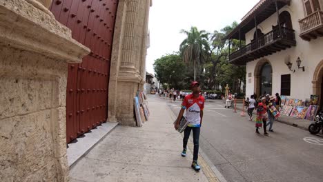 Un-Colombiano-Afroamericano-Camina-Por-Una-Calle-Del-Casco-Antiguo-De-Cartagena,-Cerca-De-Una-Enorme-Puerta-Antigua.
