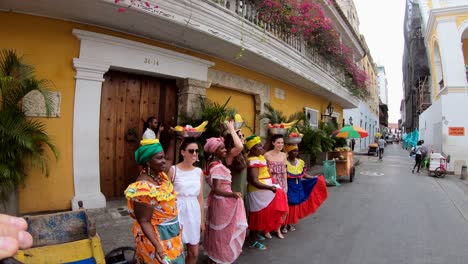 On-a-street-of-the-old-town-of-Cartagena-de-Indias,-a-group-of-tourists-poses-for-a-photo-as-they-balance-fruit-bowls-over-their-heads