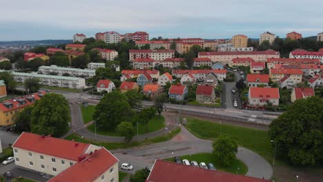 Aerial-view-over-a-suburban-area-with-lots-of-beautiful-family-friendly-houses-and-apartements,-showing-the-tram-tracks-going-around-a-tree-in-Bagaregarden-in-east-Gothenburg-in-Sweden