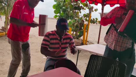 A-man-is-playing-the-caja-with-his-hands-along-his-band-members-who-play-the-Guacharaca-and-the-accordion