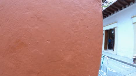 Eine-Orangefarbene-Wand-Einer-Straße-In-Der-Altstadt-Von-Cartagena-De-Indias,-Kolumbien,-Wo-Mehrere-Palenqueras-Und-Touristen-Auf-Der-Straße-Und-Dem-Bürgersteig-Stehen-Und-Gehen
