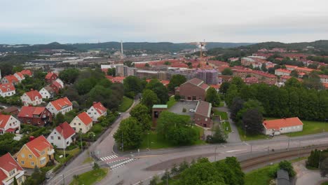 Aerial-view-of-Harlanda-church-in-Bagaregarden,-in-east-Gothenburg-in-Sweden,-with-a-suburban-area-around-it-and-different-apartement-buildings-behind-it-on-a-cloudy-day