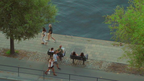 People-sitting-on-a-bench-next-to-the-water-and-pedestrians-walking-on-the-boardwalk