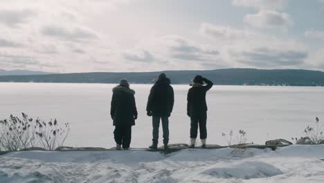 Three-People-Standing-On-Edge-Of-Frozen-White-Lake-Megantic-In-Quebec-Looking-Out