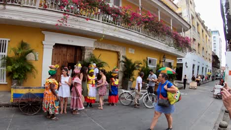 Palenqueras-and-tourists-are-talking-next-to-a-yellow-house-with-balconies-and-flowers-in-the-old-town-of-Cartagena-de-Indias,-Colombia