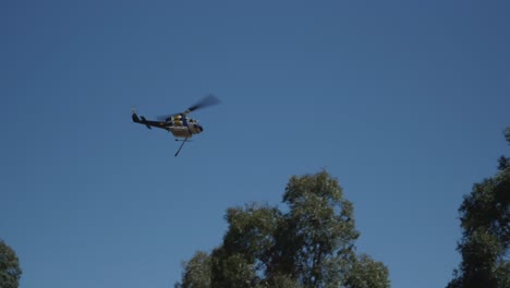 Helicopter-flying-over-tree-tops-heading-to-smoke-above-grass-fire