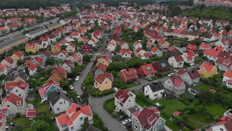 Aerial-view-over-lots-of-beautiful-family-friendly-suburban-houses-with-orange-rooftops-in-Bagaregarden-in-east-Gothenburg-in-Sweden,-with-some-nice-apartement-buildings-around-them