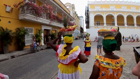 Palenqueras-dressed-with-colorful-dresses-and-balancing-bowls-of-fruit-in-their-heads-in-the-old-town-of-Cartagena-de-Indias,-Colombia