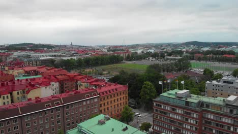 Aerial-view-over-apartement-buildings-in-Gothenburg-city,-Sweden,-with-pride-flags-waving-in-the-wind-and-a-football-field-with-people-playing-in-the-distance