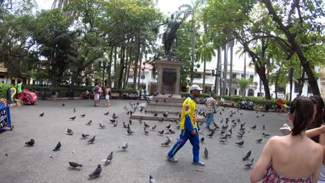 A-Colombian-wearing-a-yellow-shirt-walks-by-a-plaza-and-statue-in-the-old-town-of-Cartagena