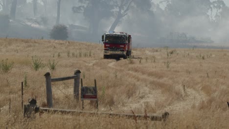 Feuerwehrauto-Fährt-Durch-Ackerland-Mit-Gelöschtem-Grasfeuer-Im-Hintergrund