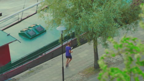 Slow-motion-view-of-man-jogging-in-early-morning-along-a-Stockholm-canal-past-boat-moored-while-looking-at-phone