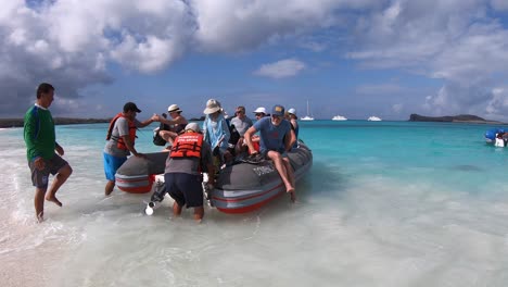 Ein-Männlicher-Tourist-Versucht,-An-Einem-Weißen-Sandstrand-Und-Im-Klaren-Wasser-Des-Ozeans-Der-Galapagos-Inseln-Von-Bord-Zu-Gehen,-Während-Menschen-Das-Boot-Festhalten