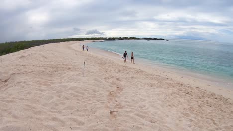 People-walking-on-a-white-sand-and-turquoise-water-beach-of-the-Galapagos-islands