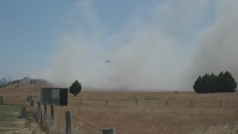 Weitwinkelaufnahme-Eines-Hubschraubers,-Der-Durch-Dichten-Rauch-über-Einem-Grasfeuer-Fliegt