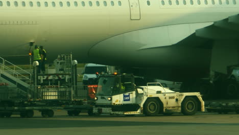 Ground-crew-in-bright-safety-vests-ready-to-access-cargo-area-of-airplane-parked-at-gate-as-trucks-with-flashing-lights-pull-up-to-collect-baggage-and-luggage-being-removed-from-underside-of-aircraft
